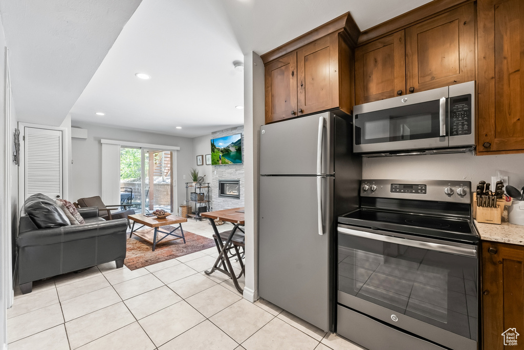 Kitchen featuring stainless steel appliances, light stone counters, a stone fireplace, and light tile floors