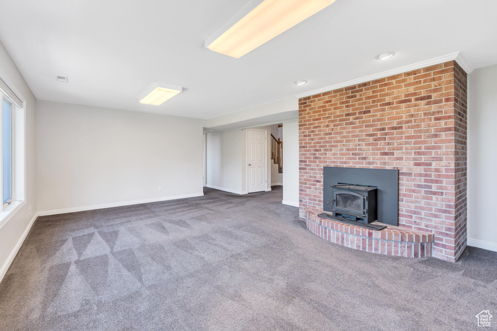 Unfurnished living room with dark colored carpet, a wood stove, and brick wall