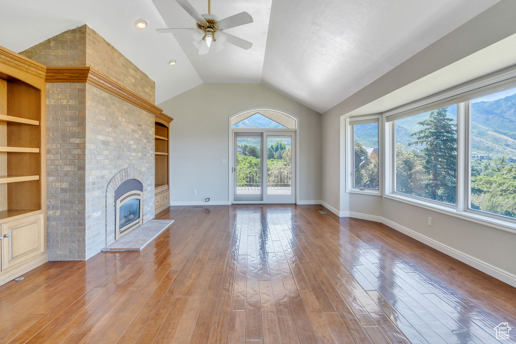 Unfurnished living room with brick wall, a fireplace, wood-type flooring, ceiling fan, and vaulted ceiling