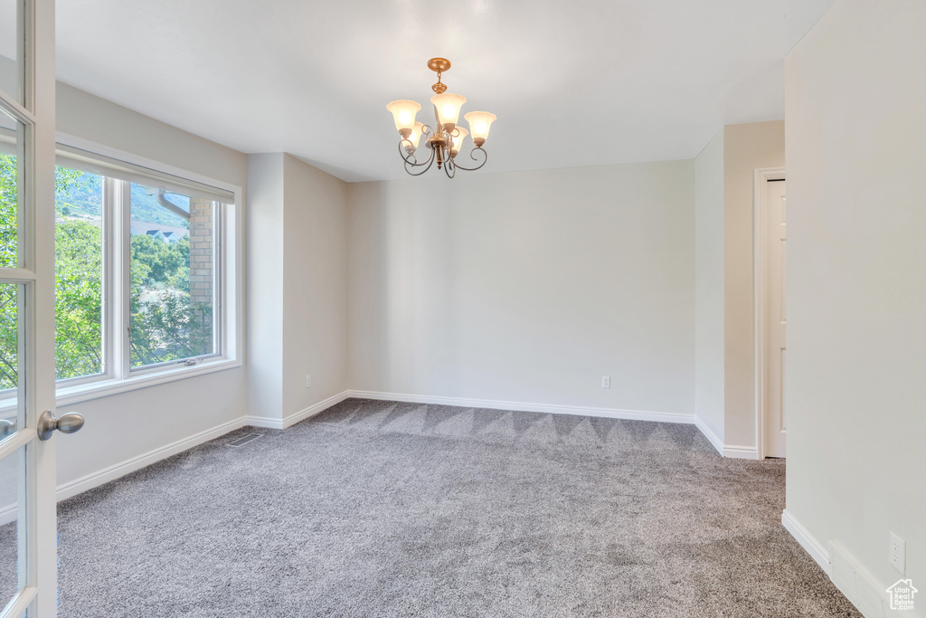 Empty room with a healthy amount of sunlight, carpet flooring, and a chandelier