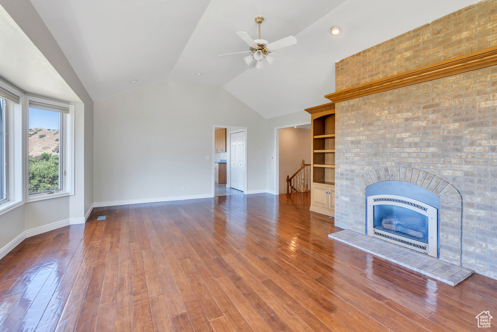 Unfurnished living room with vaulted ceiling, hardwood / wood-style floors, built in features, and ceiling fan