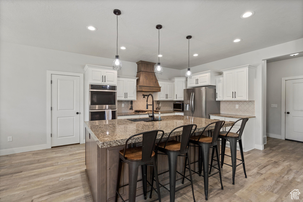 Kitchen with a kitchen breakfast bar, light hardwood / wood-style floors, tasteful backsplash, a spacious island, and appliances with stainless steel finishes