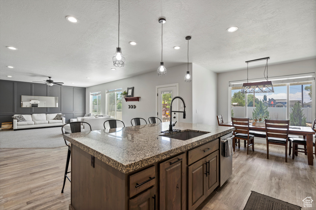 Kitchen with light hardwood / wood-style flooring, dishwasher, hanging light fixtures, a center island with sink, and sink