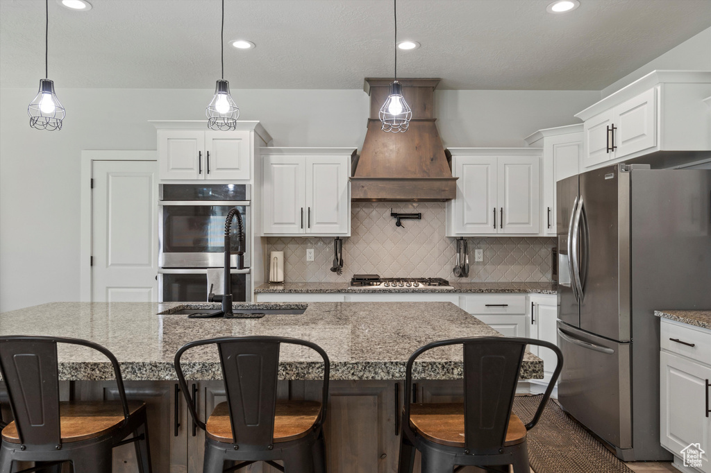 Kitchen with hanging light fixtures, appliances with stainless steel finishes, an island with sink, and premium range hood