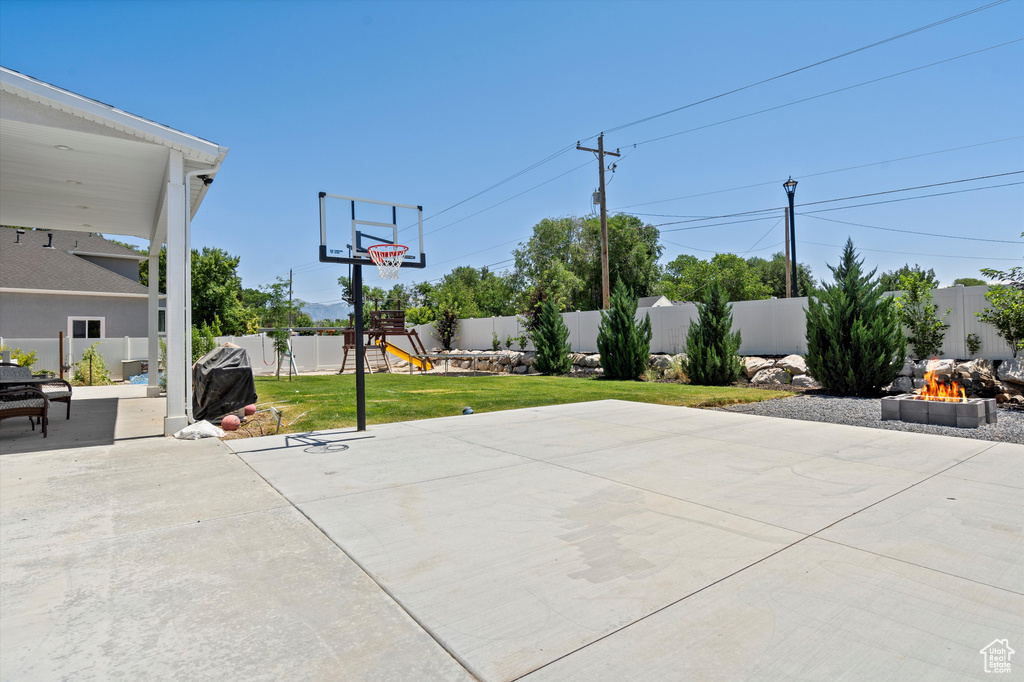 View of basketball court with a playground and a lawn