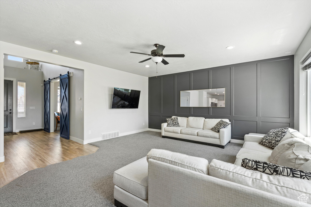 Carpeted living room featuring a barn door and ceiling fan