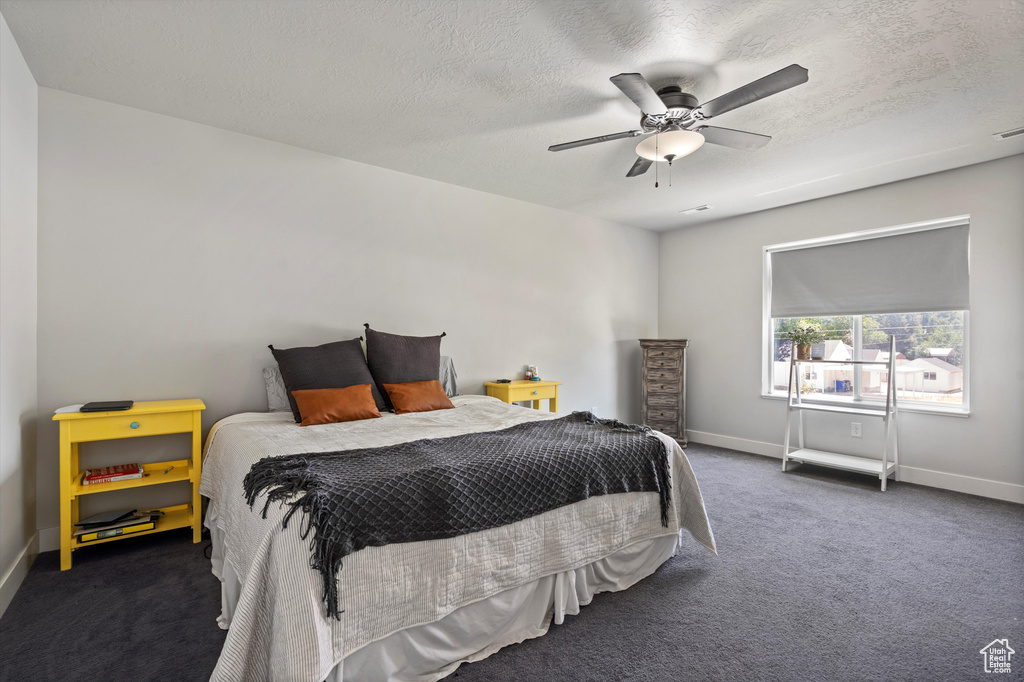 Bedroom with dark colored carpet, ceiling fan, and a textured ceiling