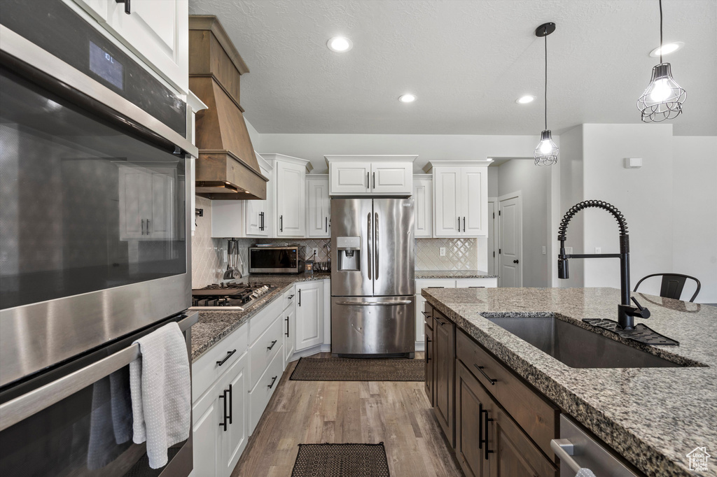 Kitchen featuring white cabinetry, stainless steel appliances, hardwood / wood-style flooring, backsplash, and sink