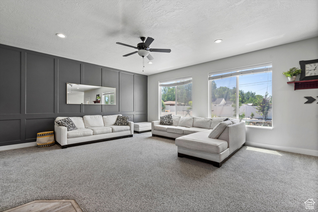 Living room with a textured ceiling, carpet flooring, and ceiling fan