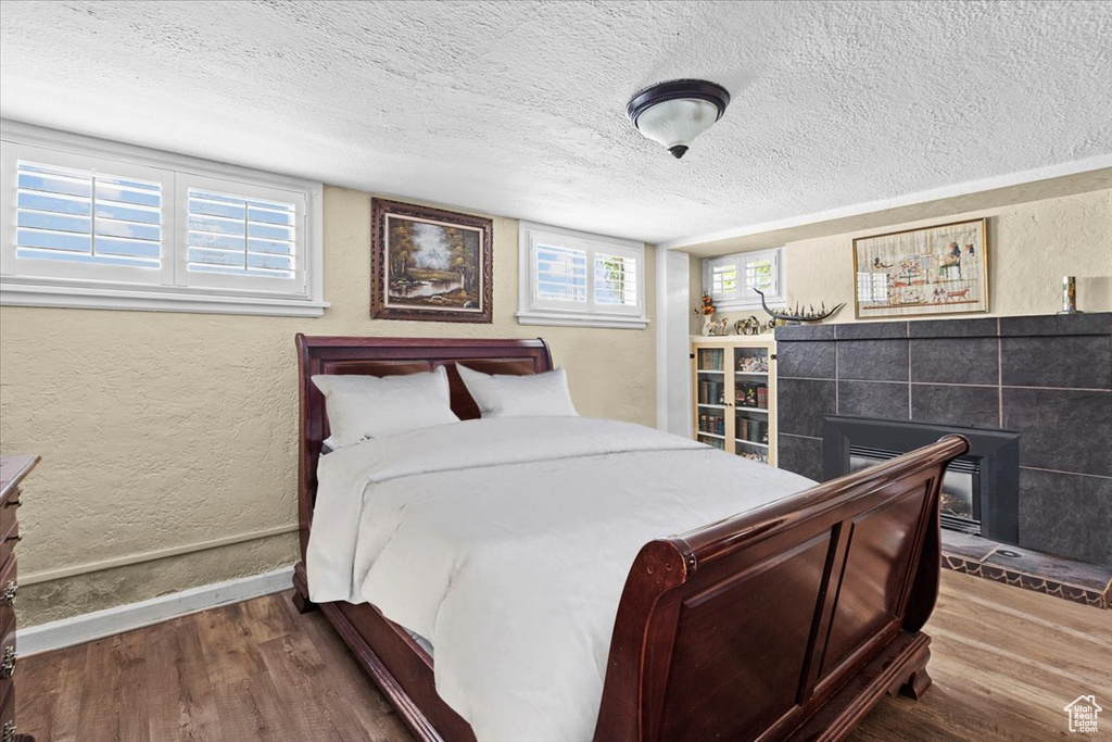 Bedroom with a textured ceiling, a tiled fireplace, and hardwood / wood-style floors