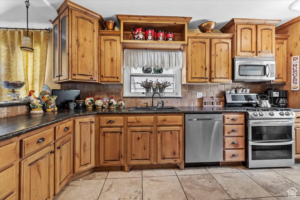 Kitchen with stainless steel appliances, light tile flooring, tasteful backsplash, and sink