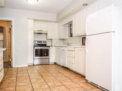 Kitchen with white cabinetry, white appliances, and light tile flooring