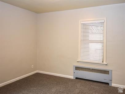 Carpeted empty room featuring radiator heating unit