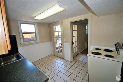 Kitchen featuring a textured ceiling, sink, white range with electric cooktop, and light tile floors