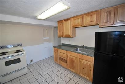 Kitchen featuring black fridge, sink, white electric range oven, and light tile floors