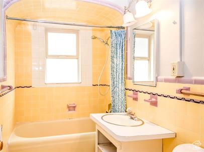 Full bathroom with vanity with extensive cabinet space, a healthy amount of sunlight, shower / bath combo, and tile walls