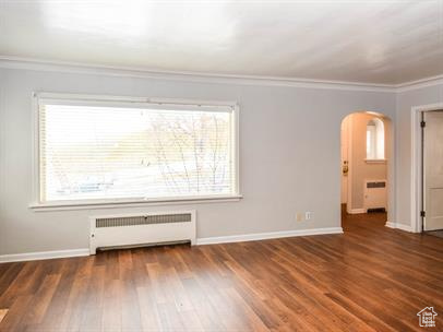 Empty room with a healthy amount of sunlight, wood-type flooring, ornamental molding, and radiator