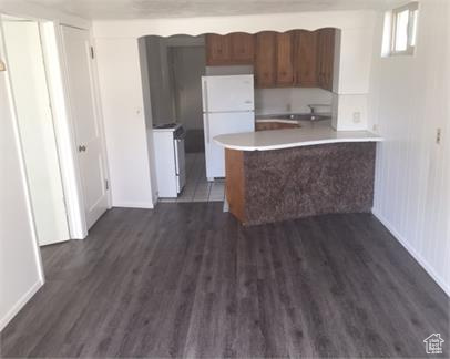 Kitchen with dark hardwood / wood-style floors, washer / dryer, kitchen peninsula, sink, and white fridge