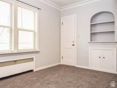 Unfurnished living room featuring carpet, crown molding, and radiator