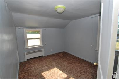 Bonus room with dark colored carpet, vaulted ceiling, and radiator