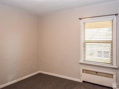 Spare room featuring radiator and dark carpet