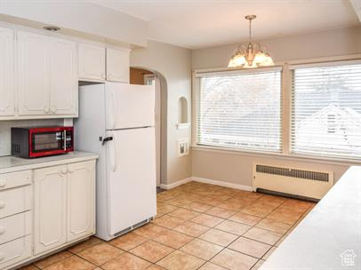 Kitchen with white refrigerator, light tile floors, radiator, and a healthy amount of sunlight