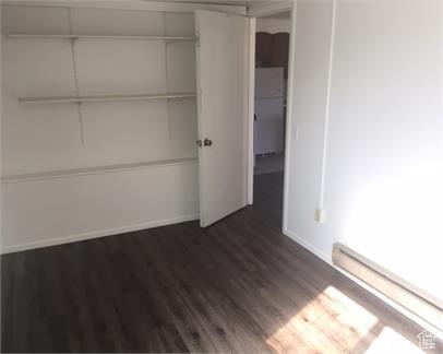 Unfurnished bedroom with a baseboard heating unit, a closet, stainless steel refrigerator, and dark wood-type flooring