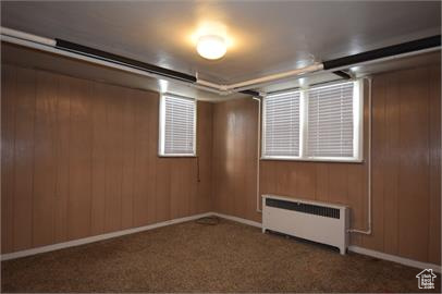 Unfurnished room featuring dark colored carpet and radiator heating unit