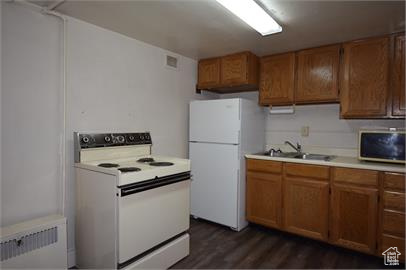 Kitchen featuring sink, white appliances, radiator, and dark hardwood / wood-style floors