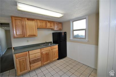 Kitchen featuring black fridge, sink, and light tile flooring