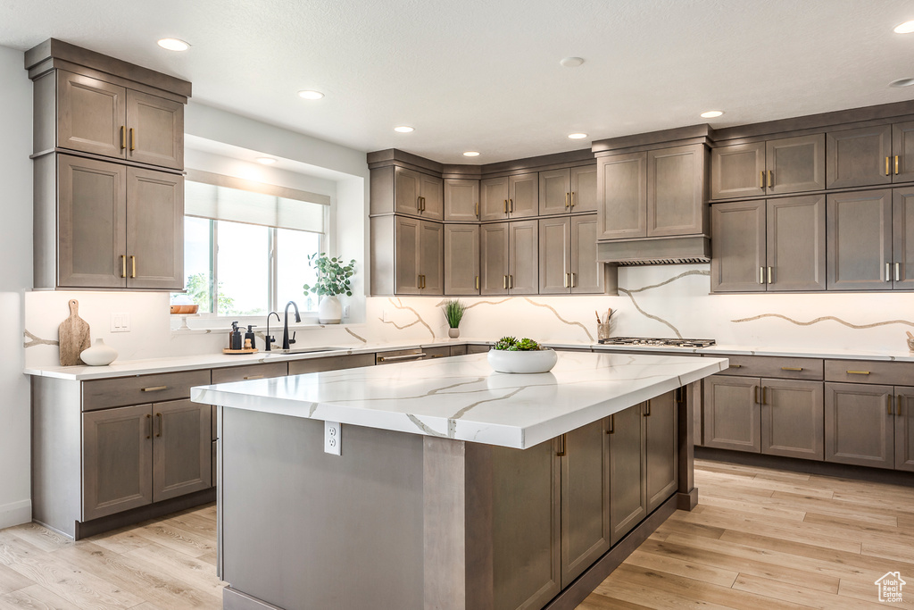 Kitchen with sink, light stone countertops, light hardwood / wood-style floors, and a kitchen island