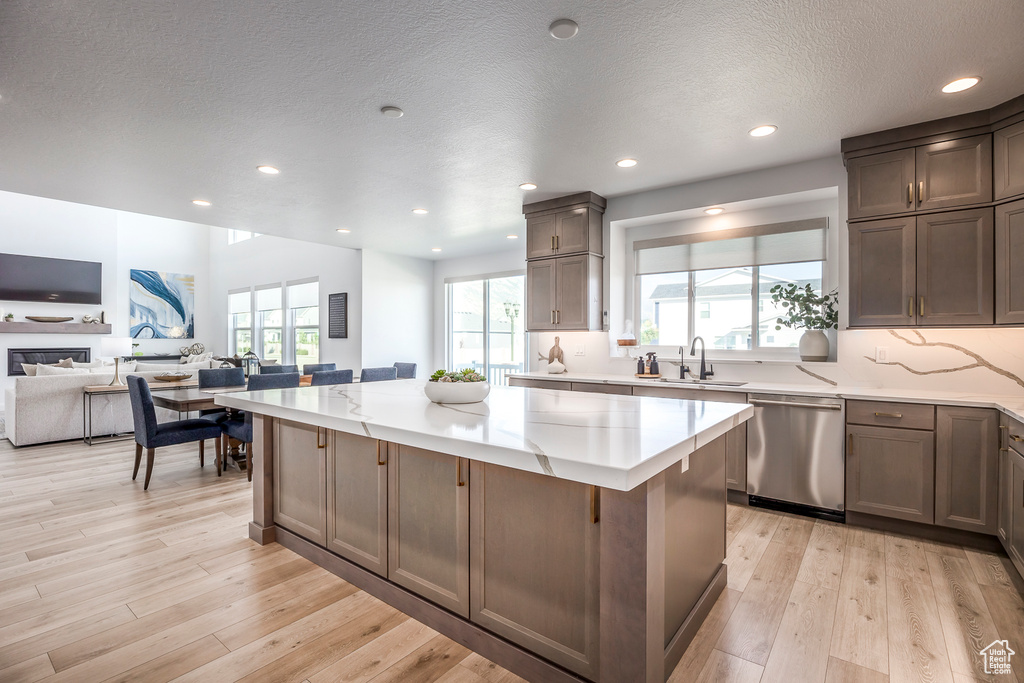 Kitchen featuring a textured ceiling, stainless steel dishwasher, light wood-type flooring, and a kitchen island