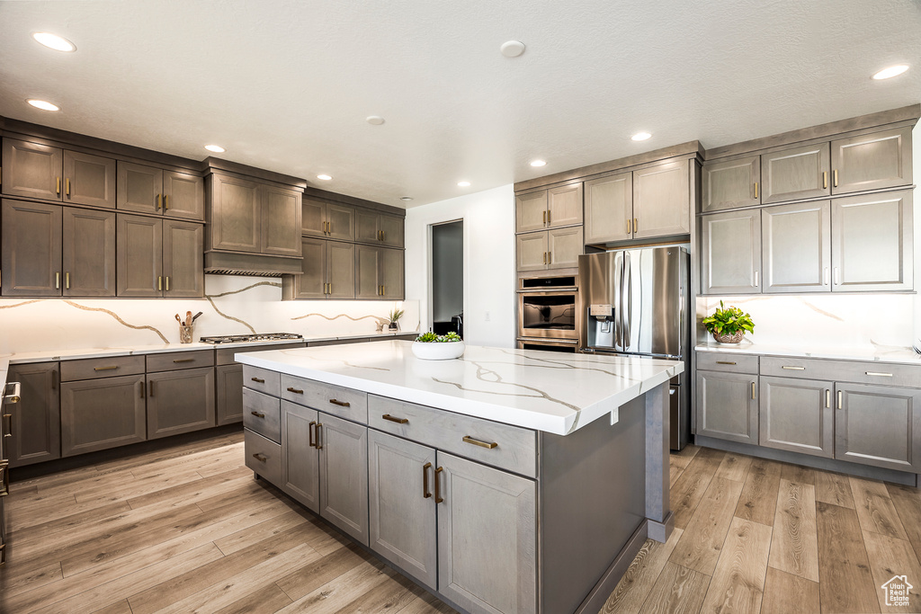 Kitchen featuring light hardwood / wood-style floors, a kitchen island, light stone counters, and stainless steel appliances