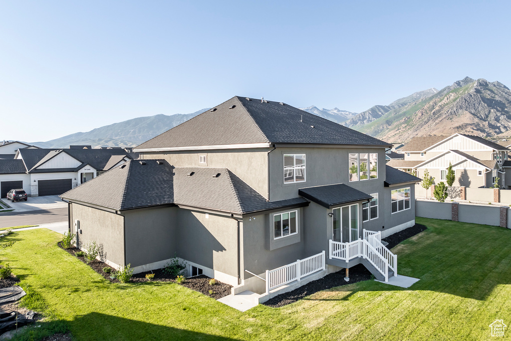 Back of property with a garage, a mountain view, and a lawn