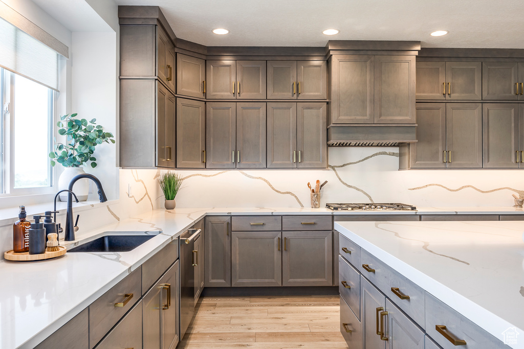 Kitchen with sink, light stone counters, light wood-type flooring, and appliances with stainless steel finishes