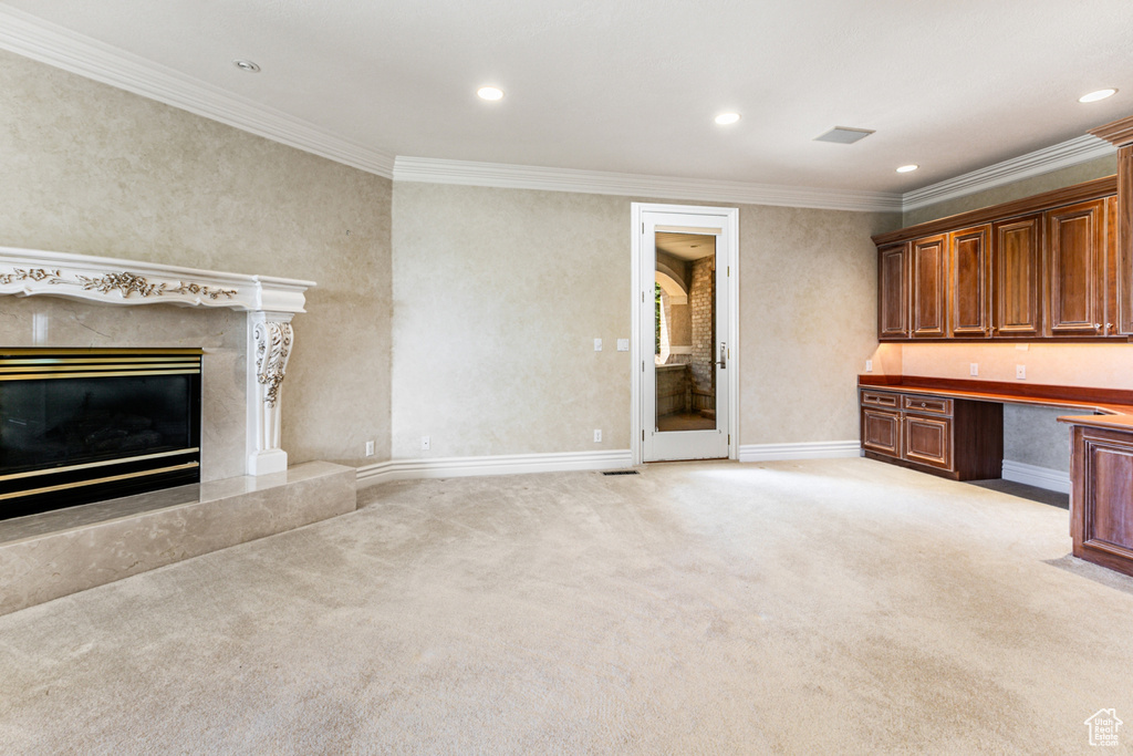 Unfurnished living room with a high end fireplace, ornamental molding, built in desk, and light carpet