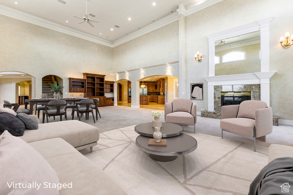 Carpeted living room with a towering ceiling, ornamental molding, ceiling fan, and a high end fireplace