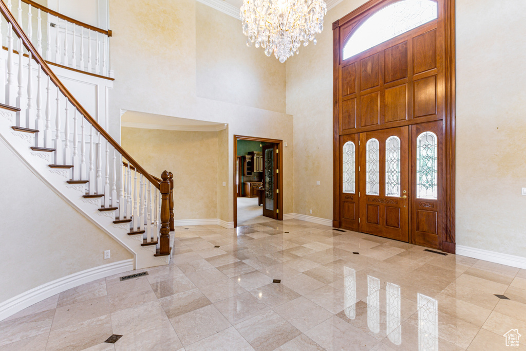 Tiled foyer entrance with a healthy amount of sunlight, an inviting chandelier, a towering ceiling, and ornamental molding