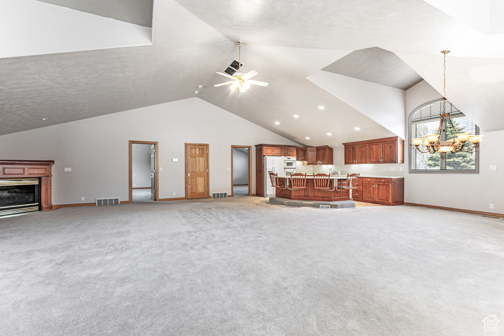 Unfurnished living room featuring ceiling fan with notable chandelier, vaulted ceiling, light colored carpet, and sink