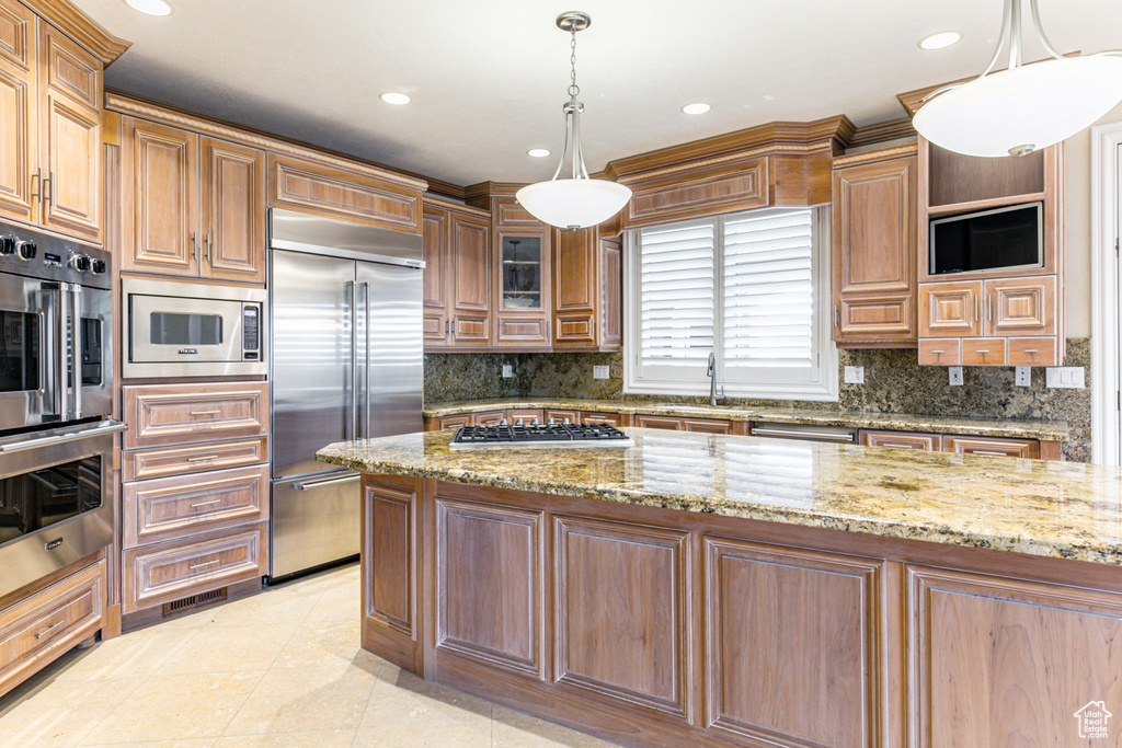 Kitchen featuring light tile flooring, backsplash, hanging light fixtures, built in appliances, and light stone countertops