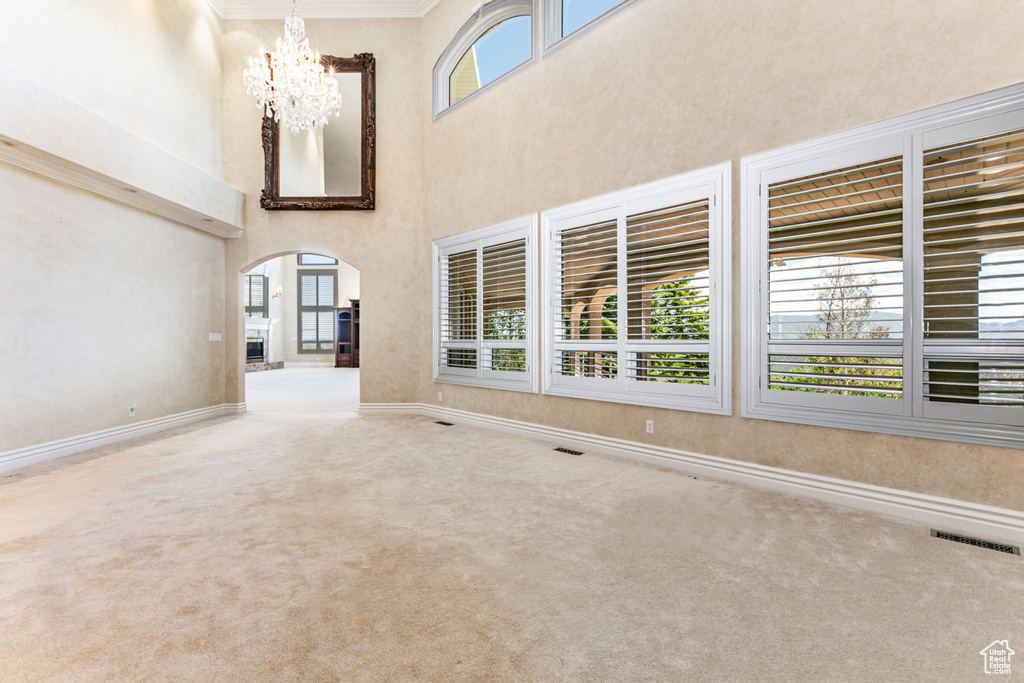 Unfurnished living room with carpet flooring, a towering ceiling, ornamental molding, and a chandelier