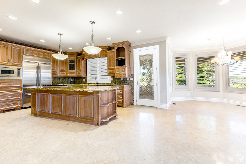 Kitchen featuring light stone countertops, built in appliances, backsplash, hanging light fixtures, and ornamental molding