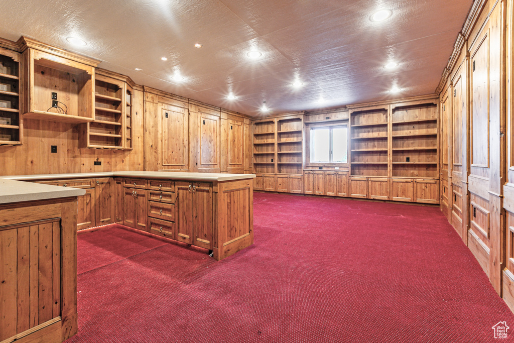 Kitchen with built in features, dark colored carpet, kitchen peninsula, and wood walls