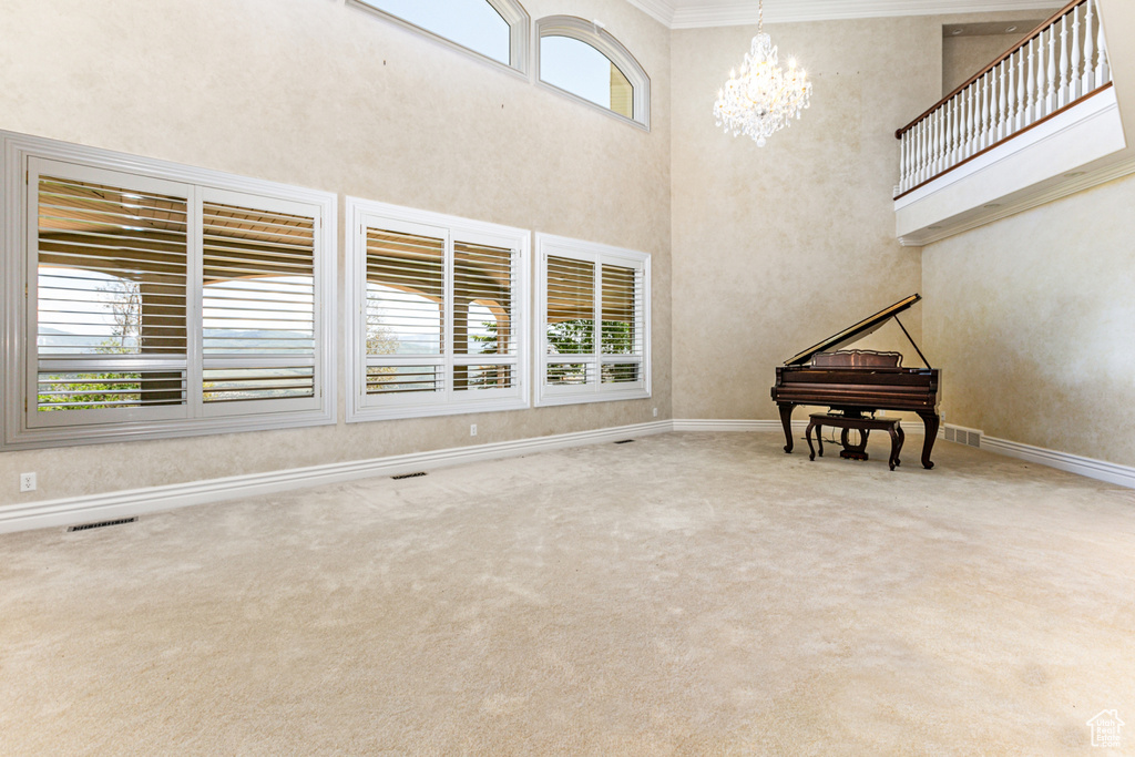 Unfurnished living room with plenty of natural light, an inviting chandelier, crown molding, and carpet flooring