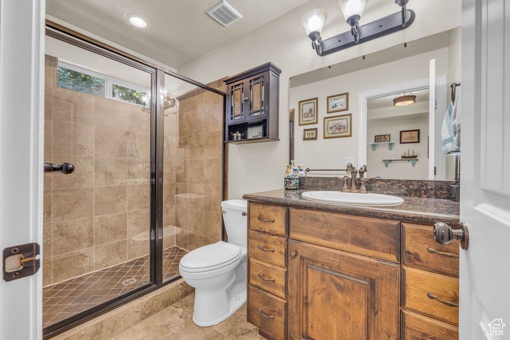 Bathroom featuring toilet, tile floors, a shower with shower door, large vanity, and a textured ceiling