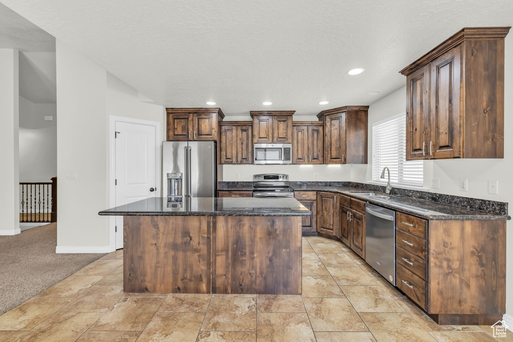 Kitchen featuring a kitchen island, light carpet, appliances with stainless steel finishes, sink, and dark stone countertops