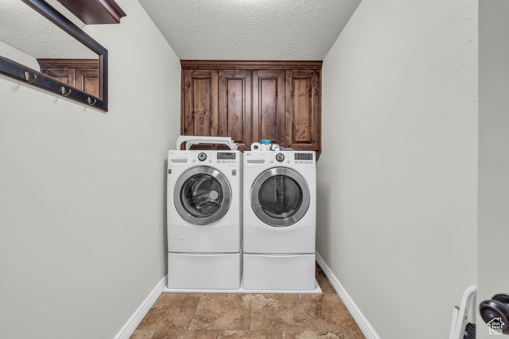 Laundry area with washing machine and clothes dryer, cabinets, and a textured ceiling