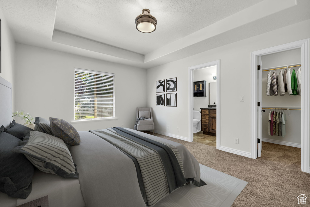 Carpeted bedroom with ensuite bathroom, a walk in closet, a closet, a raised ceiling, and a textured ceiling