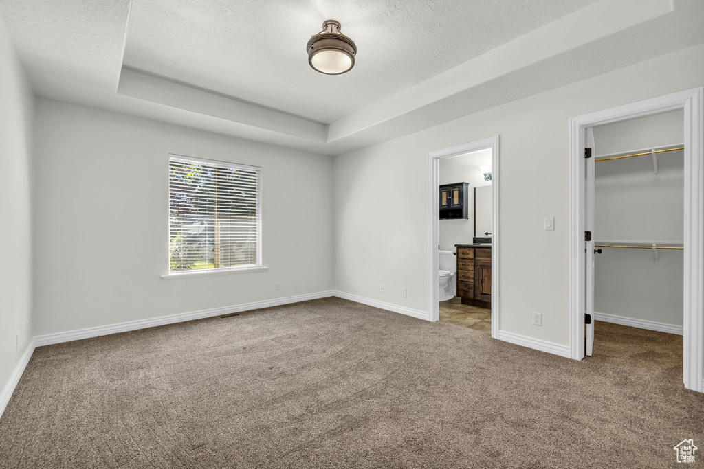 Unfurnished bedroom featuring light carpet, a closet, a tray ceiling, a walk in closet, and ensuite bathroom