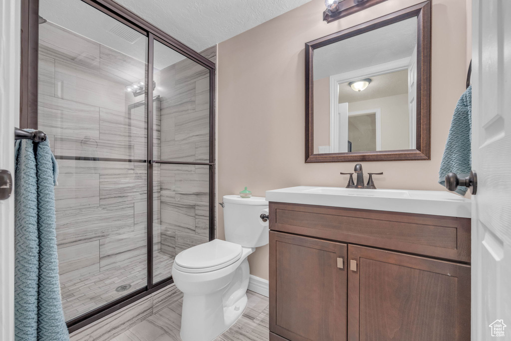 Bathroom featuring a shower with door, tile flooring, toilet, and vanity